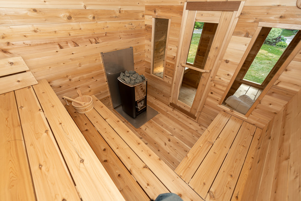 Georgian cabin sauna room from above with L-shaped cedar benches, wood-burning heater and bucket