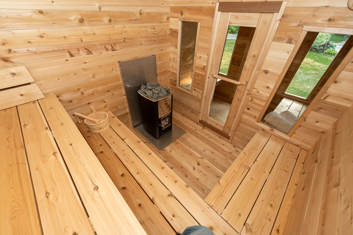 Georgian cabin sauna room from above with L-shaped cedar benches, wood-burning heater and bucket